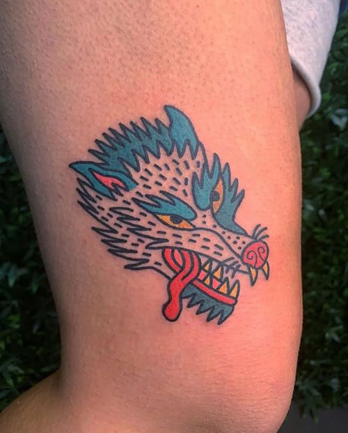 Foto van een tatoeage van een ingekleurde draak op het bovenbeen.