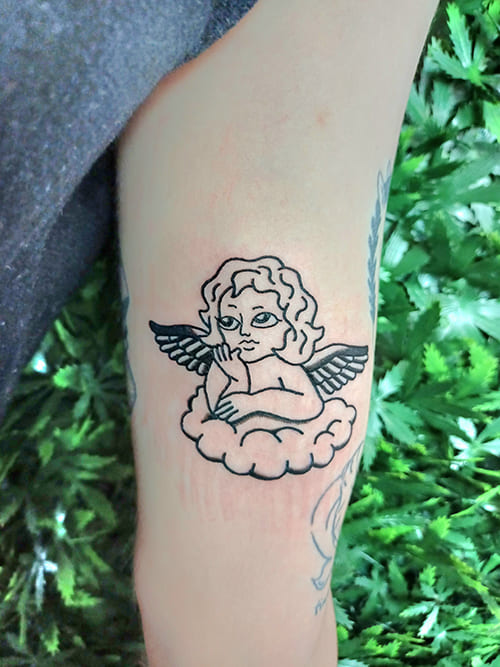 Foto van een illustratieve tattoo van een engeltje op een wolk.
