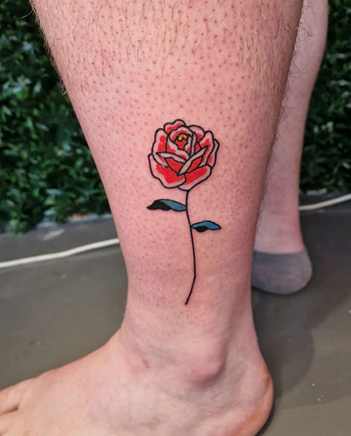 Foto van een tatoeage van een ingekleurde roos op het onderbeen.