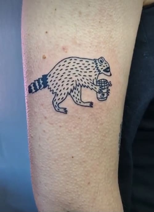 Foto van een illustratieve tattoo van een wasbeer op de bovenarm.