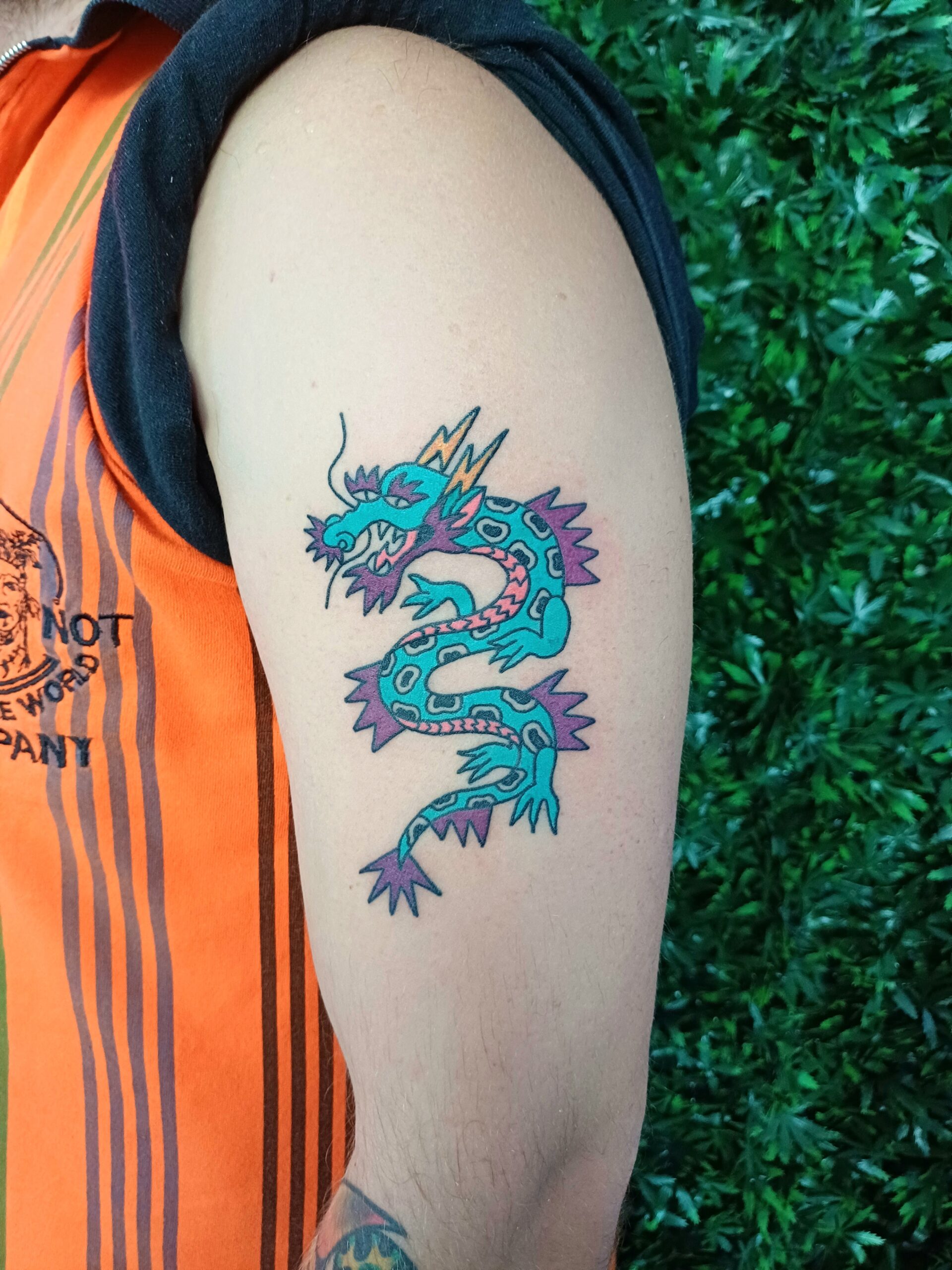 Foto van een tatoeage van een ingekleurde draak op de bovenarm.