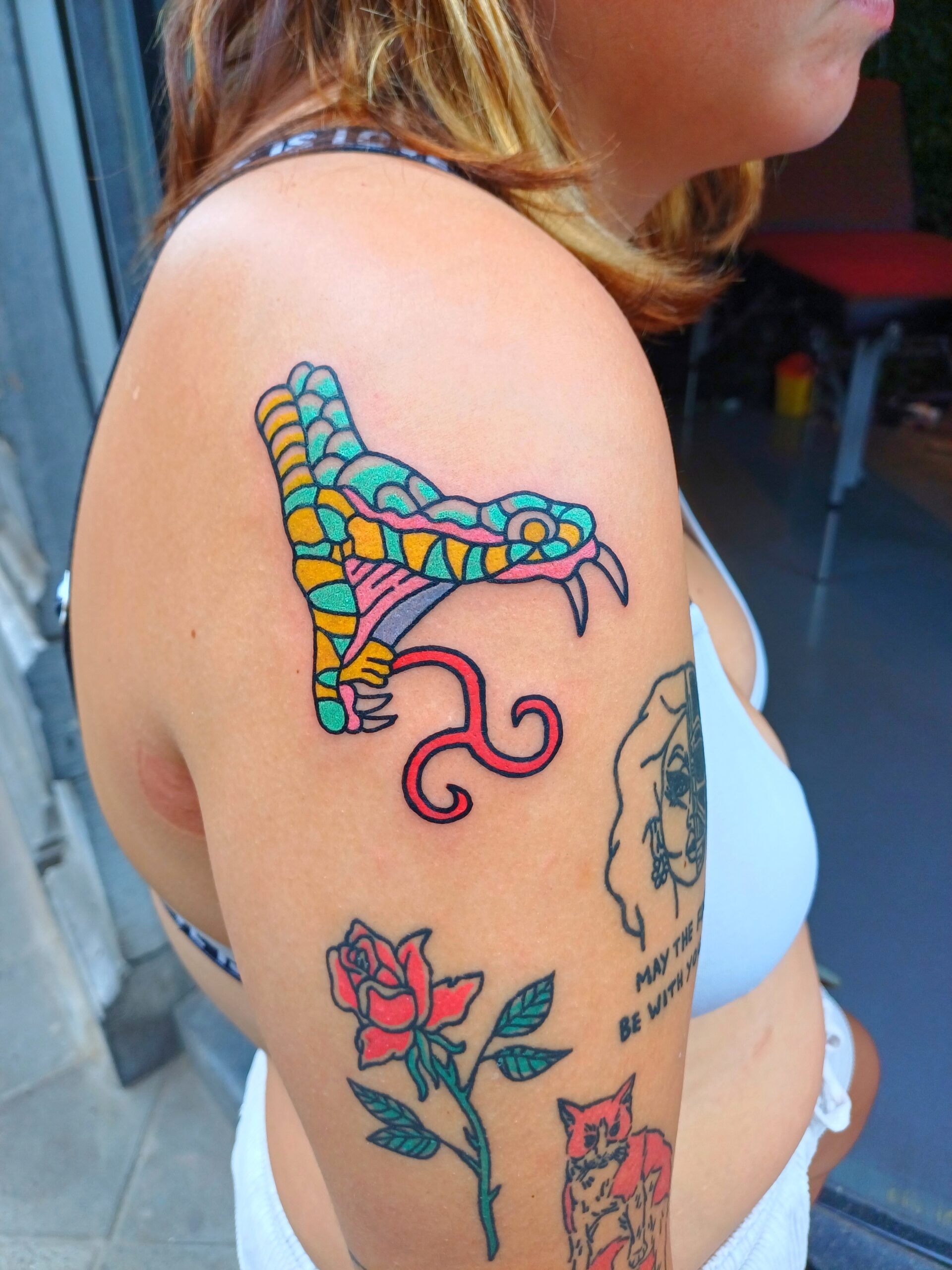 Foto van een tatoeage van een ingekleurde slangenkop op de bovenarm.